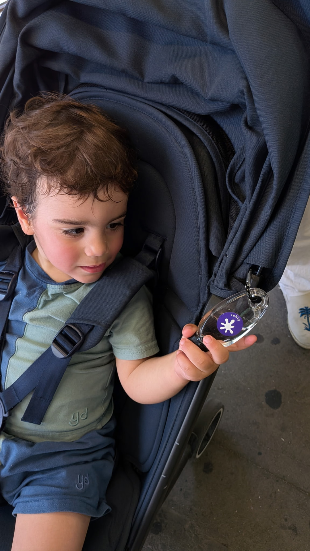 A toddler in a stroller holding an Ickly pocket hand sanitizer with a school QR tag