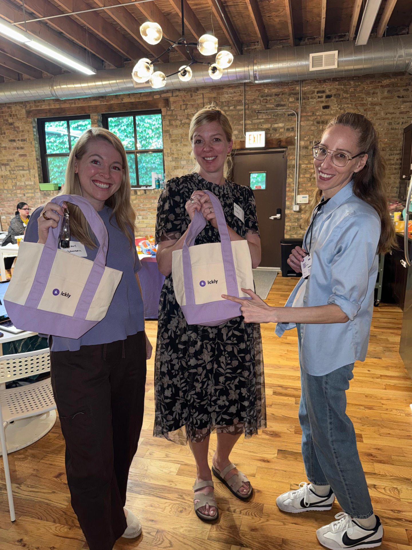 Three attendees holding lavender and canvas Ickly tote bags