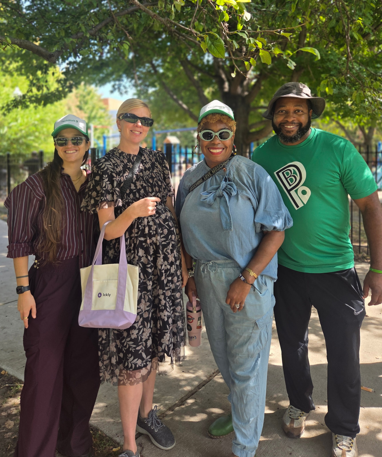 Four Family TechWalk attendees posing together in a park, one holding a lavender Ickly tote bag