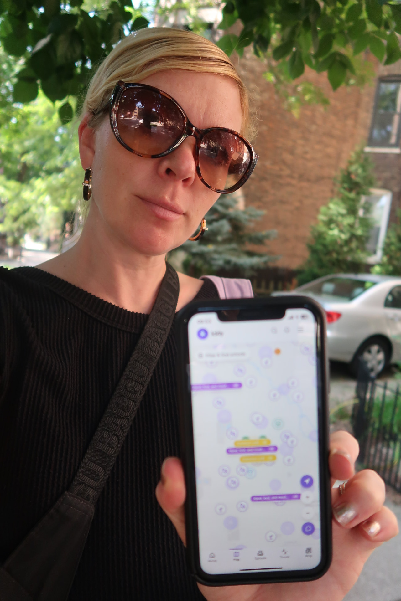 A parent holding her phone outdoors, showing the Ickly app while standing near a school